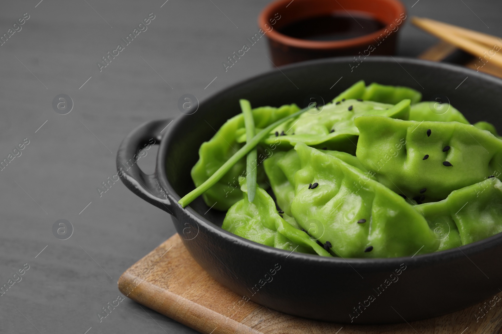 Photo of Delicious green dumplings (gyozas) and soy sauce on grey wooden table, closeup. Space for text