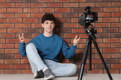 Photo of Smiling teenage blogger explaining something while streaming indoors