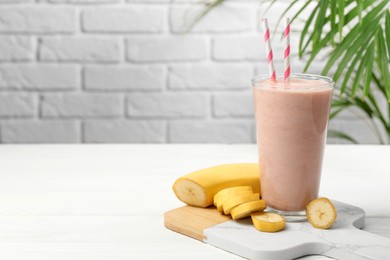 Photo of Glass of tasty banana smoothie with straws and fresh fruit on white wooden table. Space for text