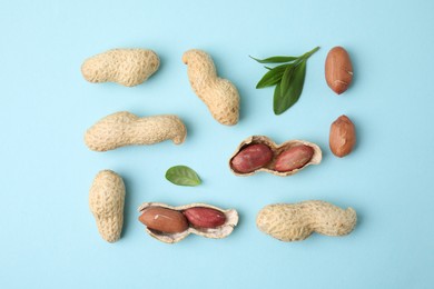 Fresh peanuts and leaves on light blue table, flat lay