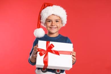 Happy little child in Santa hat with gift box on red background. Christmas celebration