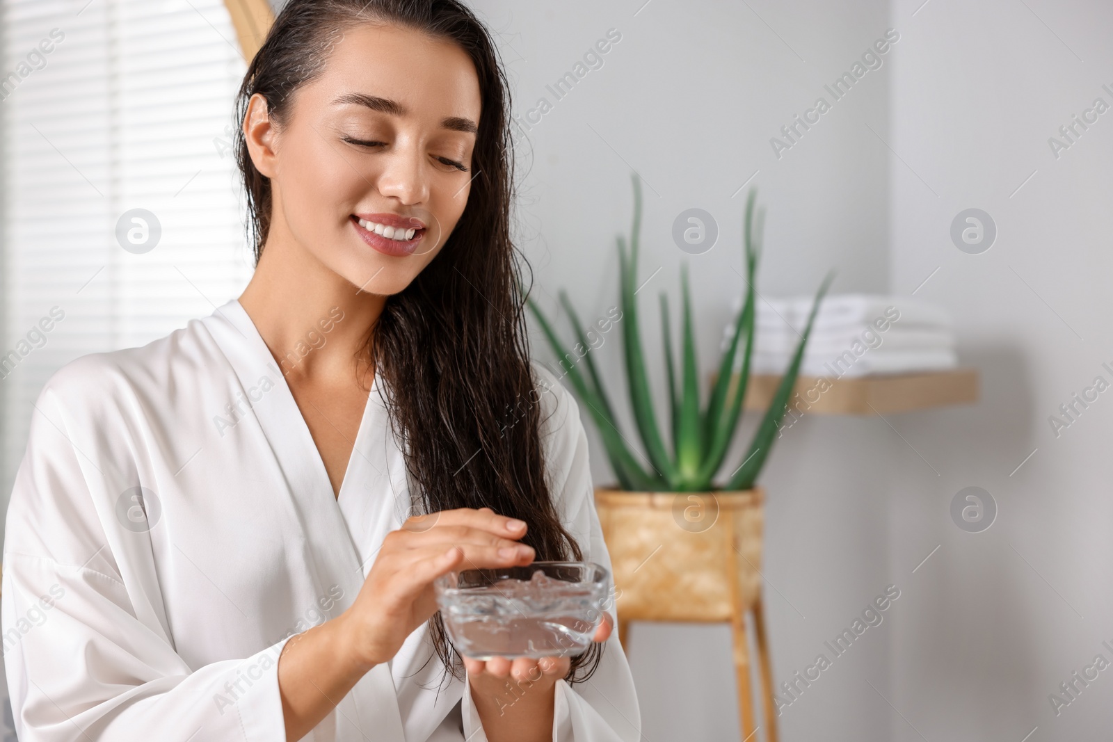 Photo of Young woman holding bowl of aloe hair mask in bathroom. Space for text