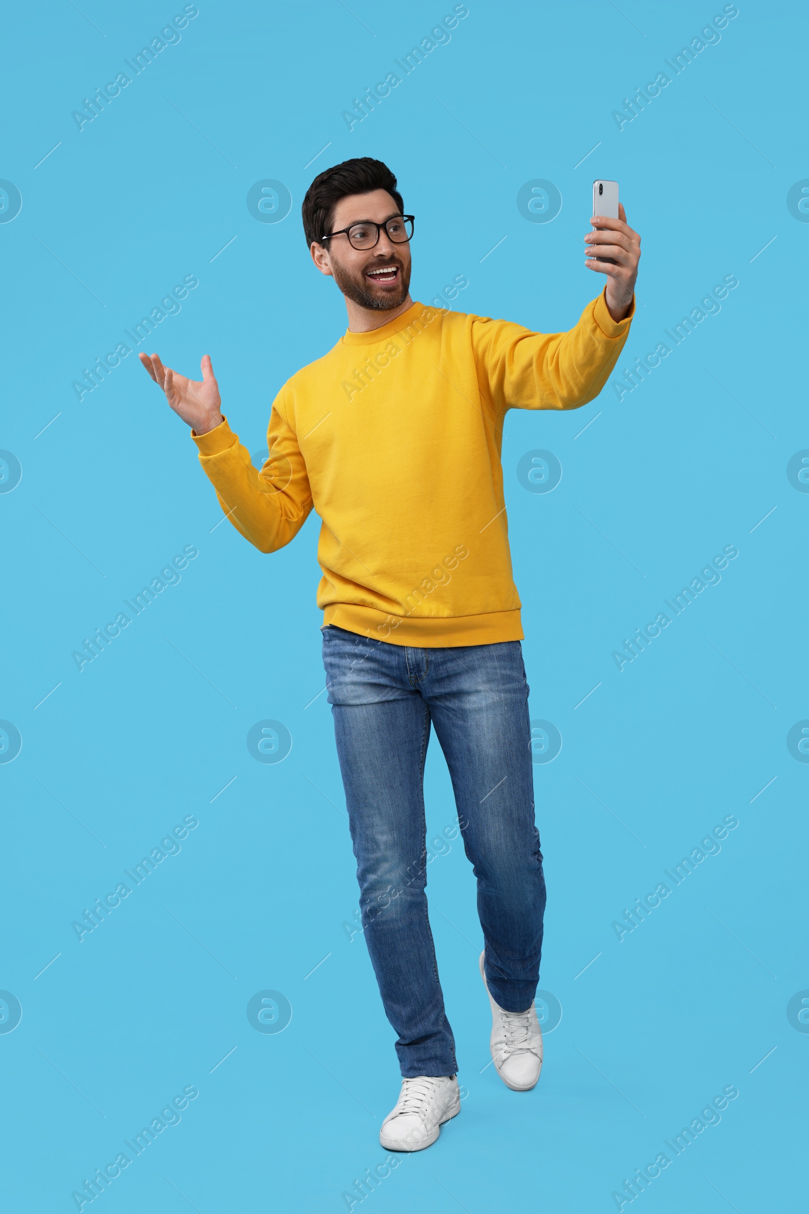 Photo of Smiling man taking selfie with smartphone on light blue background