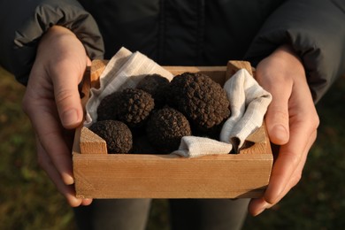Photo of Woman holding wooden crate with truffles outdoors, closeup