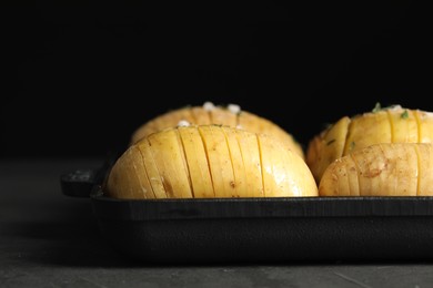 Photo of Raw Hasselback potatoes in baking pan on dark grey table, closeup