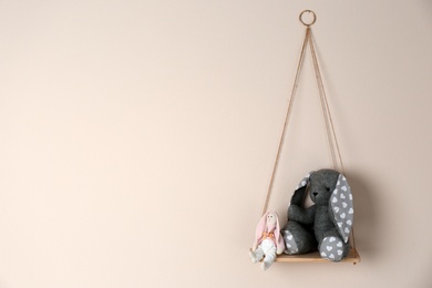 Shelf with cute toy bunnies on beige wall, space for text. Child's room interior element