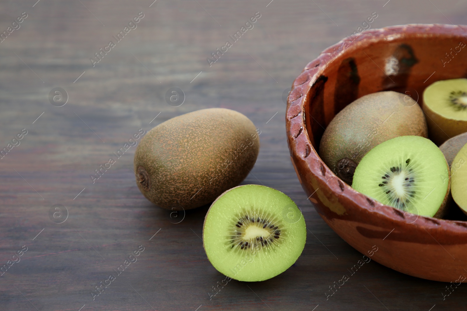 Photo of Whole and cut fresh kiwis on wooden table, closeup. Space for text