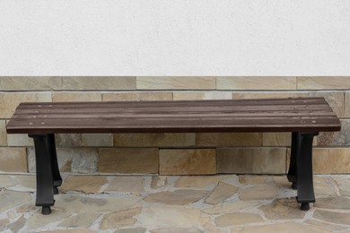 Photo of Wooden bench near wall with stone fragments outdoors