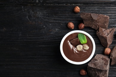 Dessert bowl with sweet chocolate cream, nuts and chunks on wooden table, flat lay. Space for text