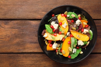 Photo of Delicious persimmon salad with pomegranate and spinach on wooden table, top view. Space for text