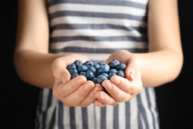 Woman holding juicy fresh blueberries on black background, closeup