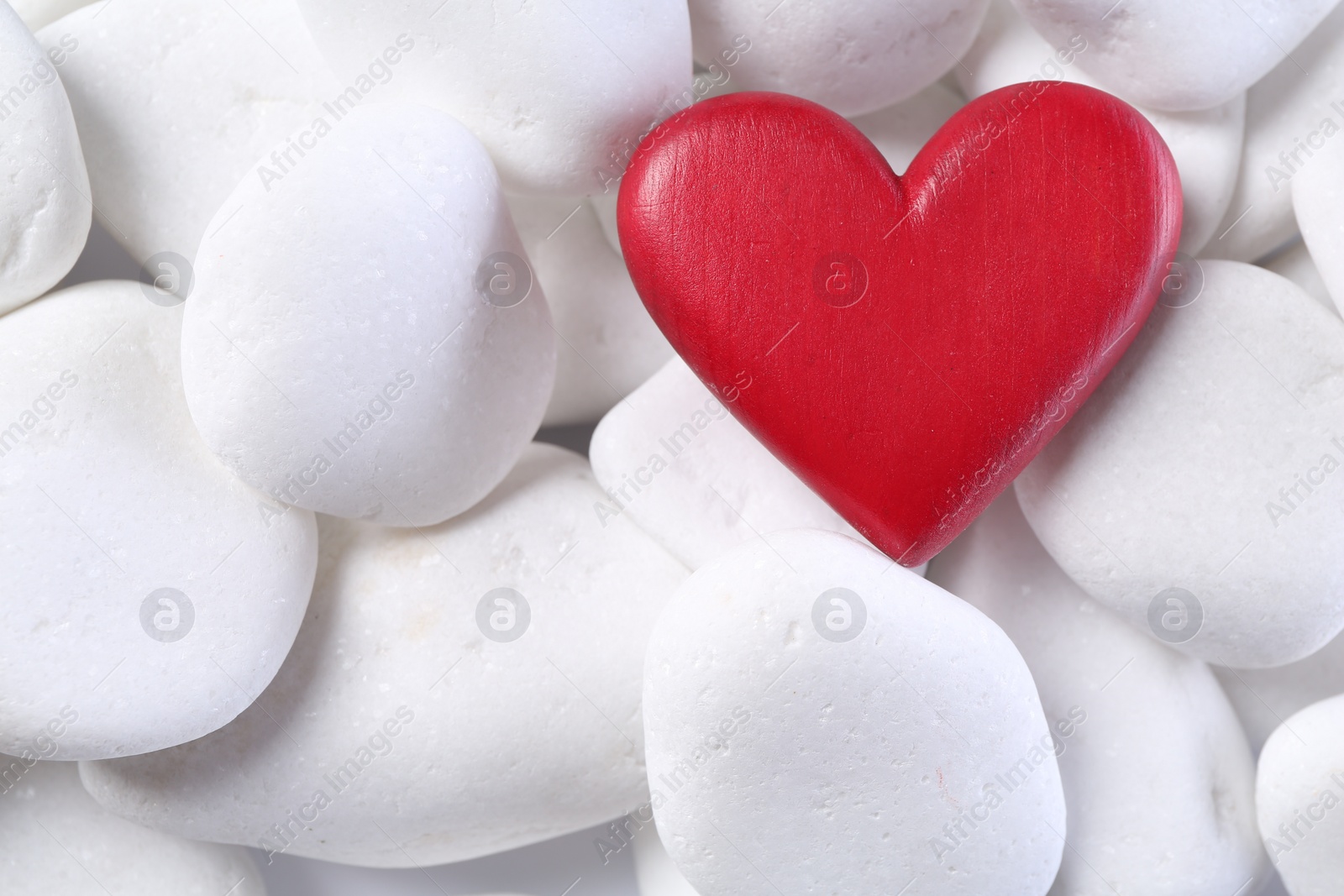 Photo of Decorative heart on white pebble stones, top view