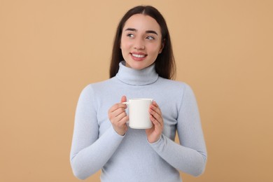 Photo of Happy young woman holding white ceramic mug on beige background