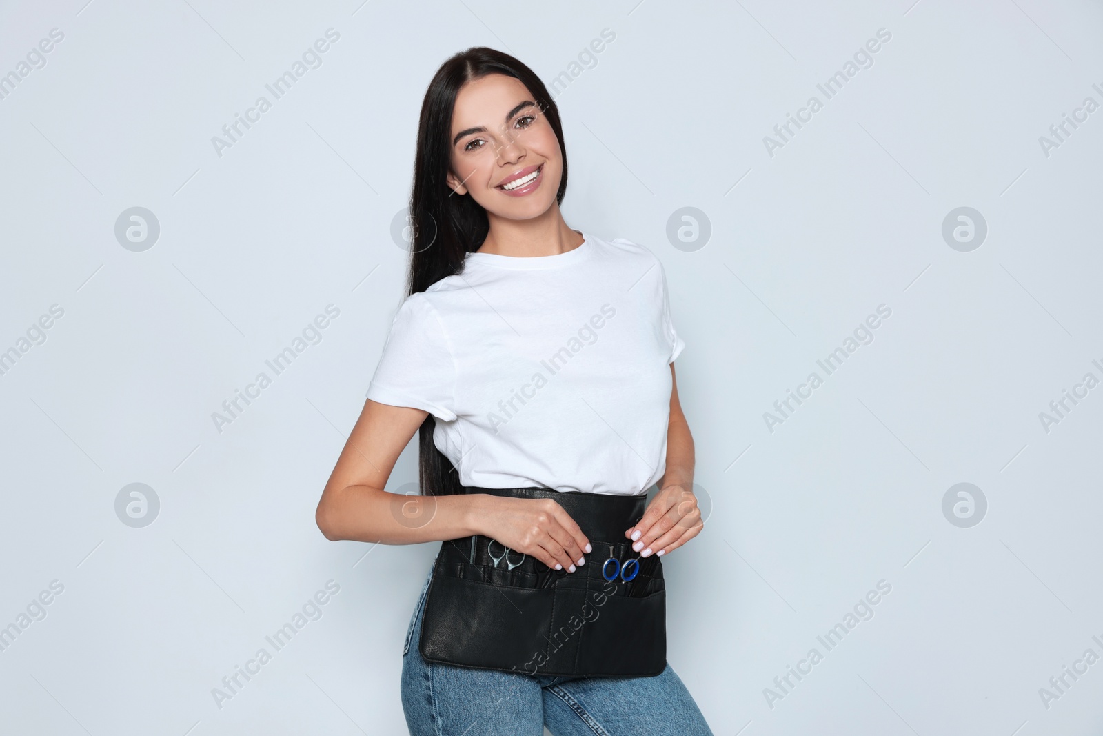 Photo of Portrait of happy hairdresser with professional tools on light background
