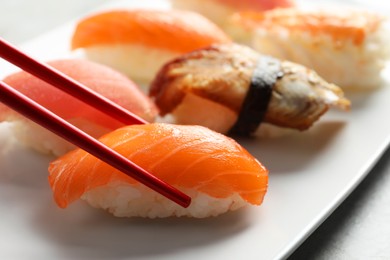 Taking delicious nigiri sushi with chopsticks from plate on grey table, closeup