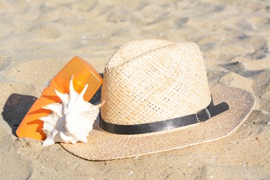 Photo of Stylish straw hat, sea shell and sunscreen on sandy beach
