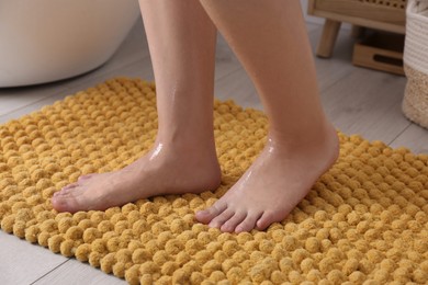Photo of Woman standing on soft yellow bath mat near tub at home, closeup