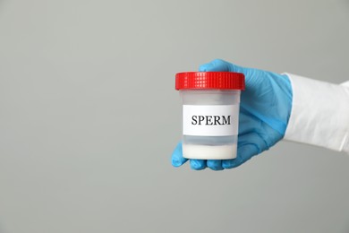 Photo of Scientist holding container with sperm on grey background, closeup. Space for text