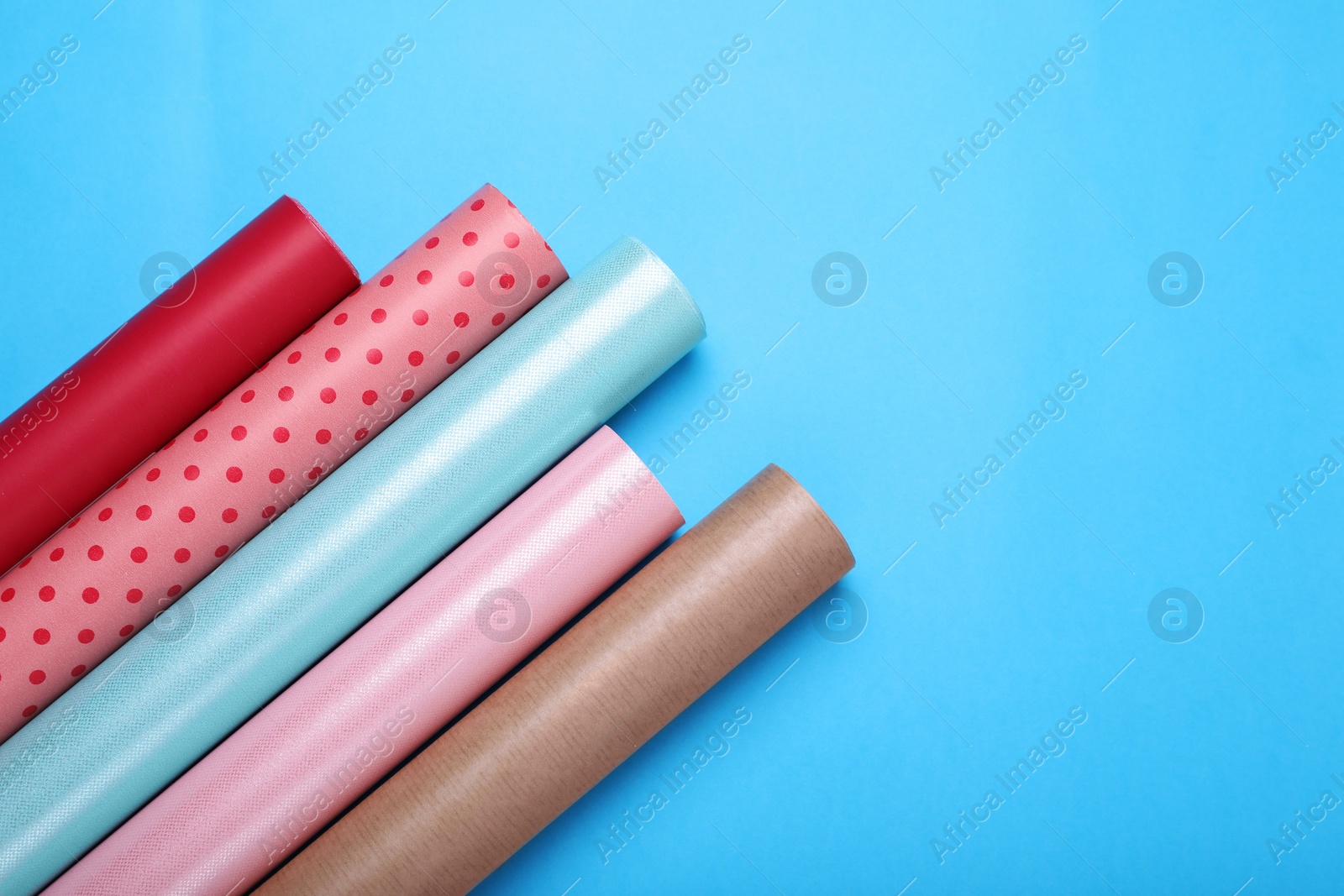 Photo of Rolls of wrapping papers on light blue background, flat lay. Space for text