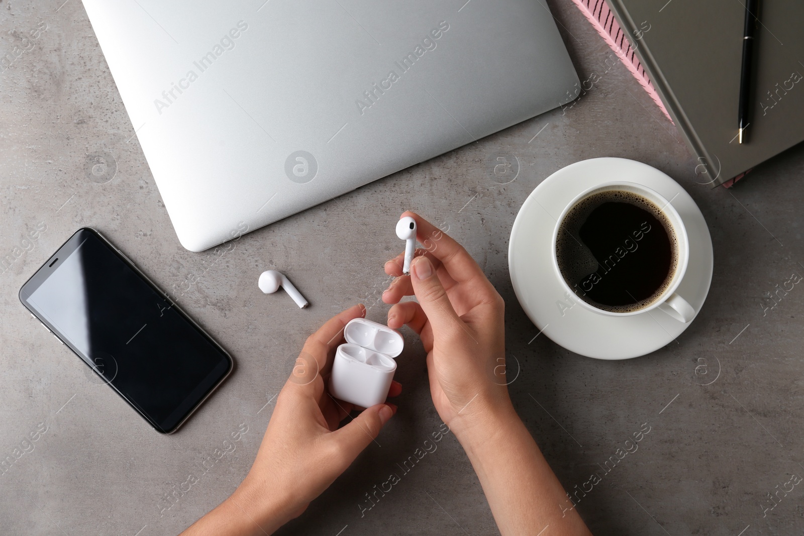 Photo of Woman putting wireless earphones in charging case at grey stone table, top view