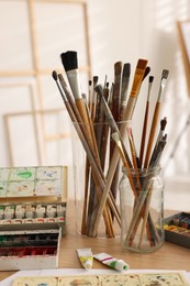Different brushes and colorful paints on wooden table in studio. Artist's workplace