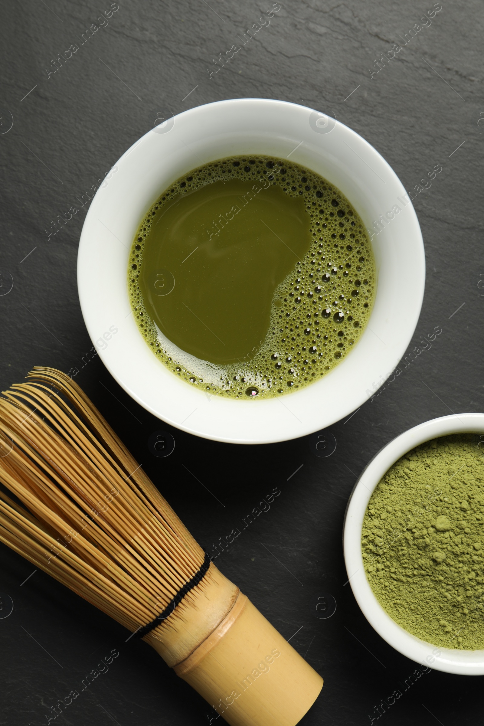 Photo of Fresh matcha tea, green powder and bamboo whisk on black table, flat lay