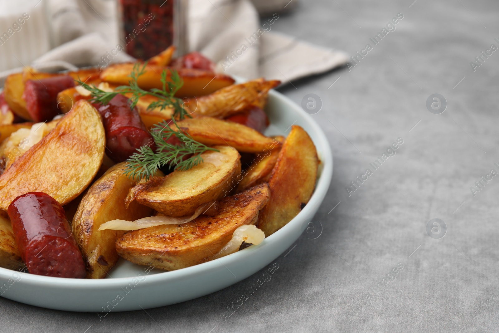 Photo of Delicious baked potato with thin dry smoked sausages, onion and dill on gray table, closeup. Space for text