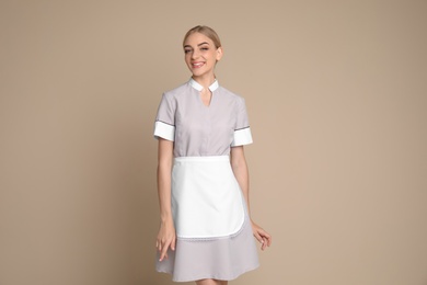 Photo of Portrait of young chambermaid in tidy uniform on color background