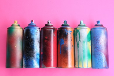 Photo of Many spray paint cans on pink background, flat lay