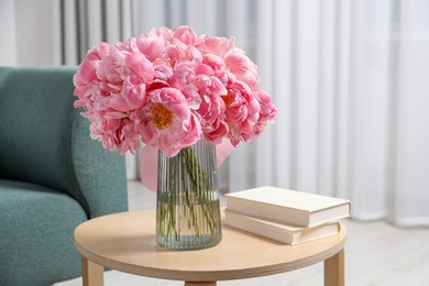 Beautiful bouquet of pink peonies in vase and books on wooden table indoors