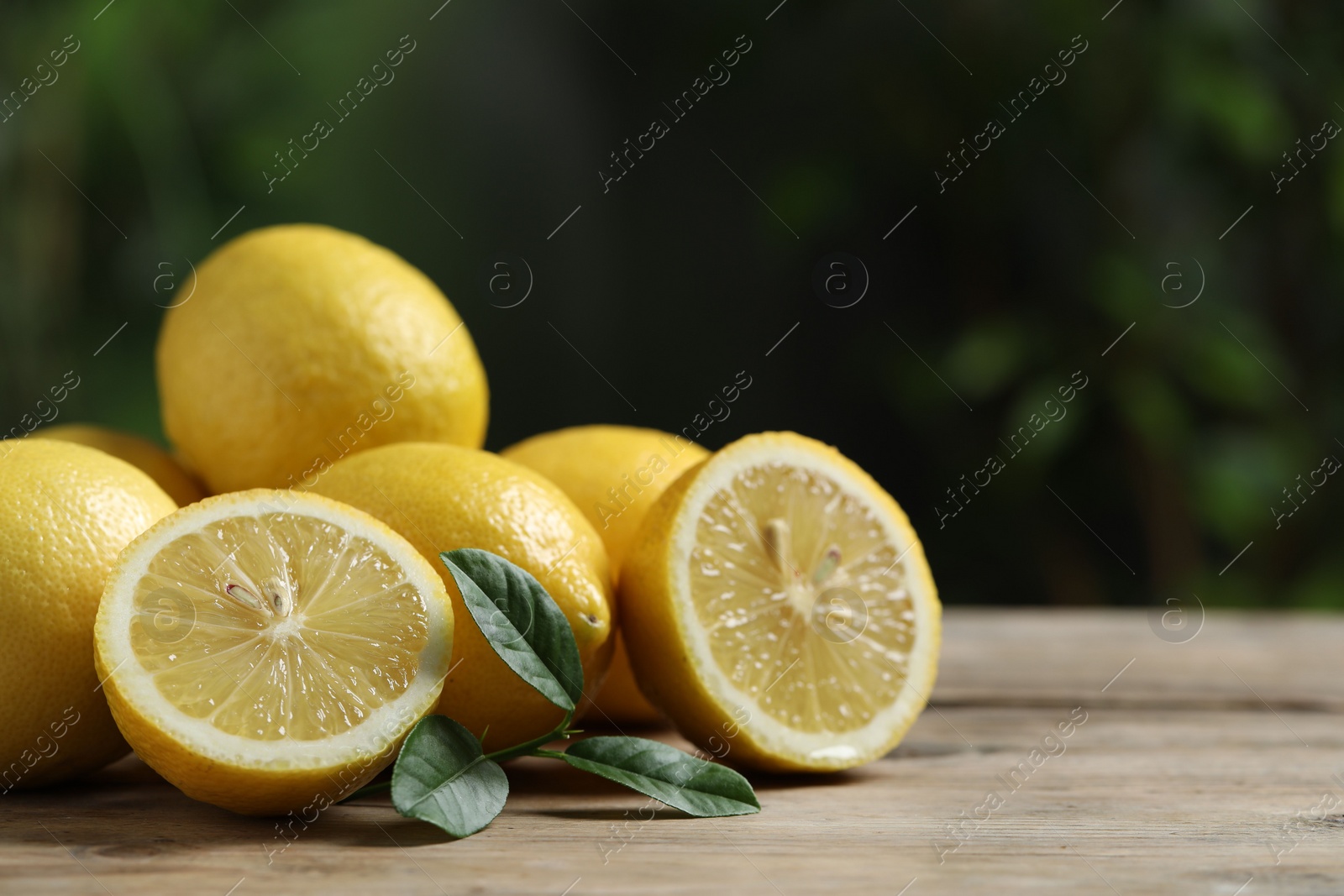 Photo of Fresh lemons and green leaves on wooden table, closeup. Space for text