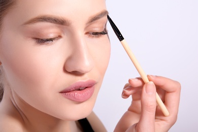 Photo of Beautiful woman with perfect eyebrows applying makeup on light background