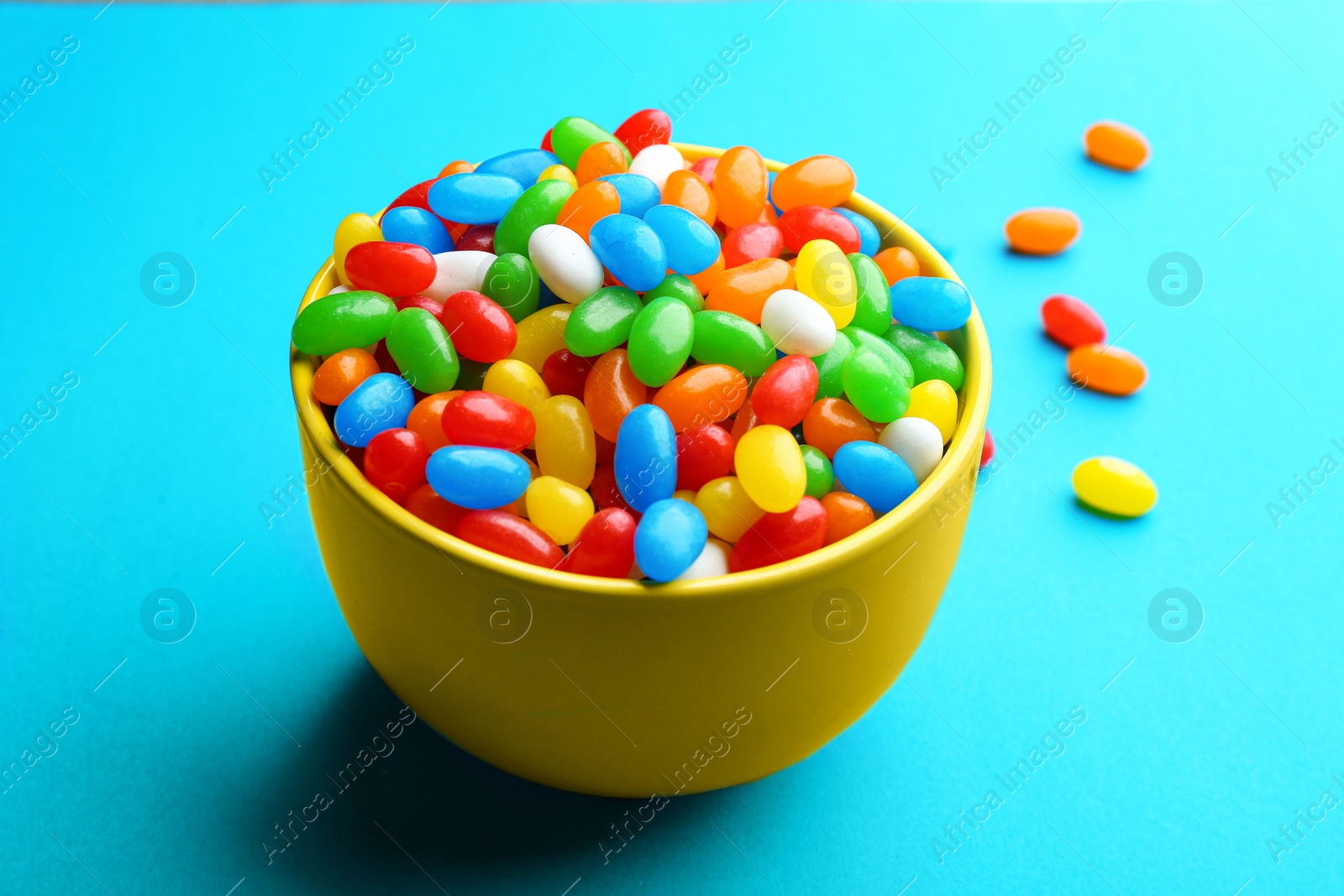 Photo of Bowl with colorful jelly beans on turquoise background