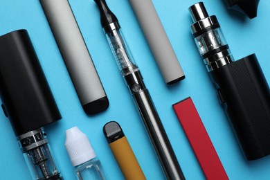 Different electronic cigarettes and liquid solution on light blue background, flat lay