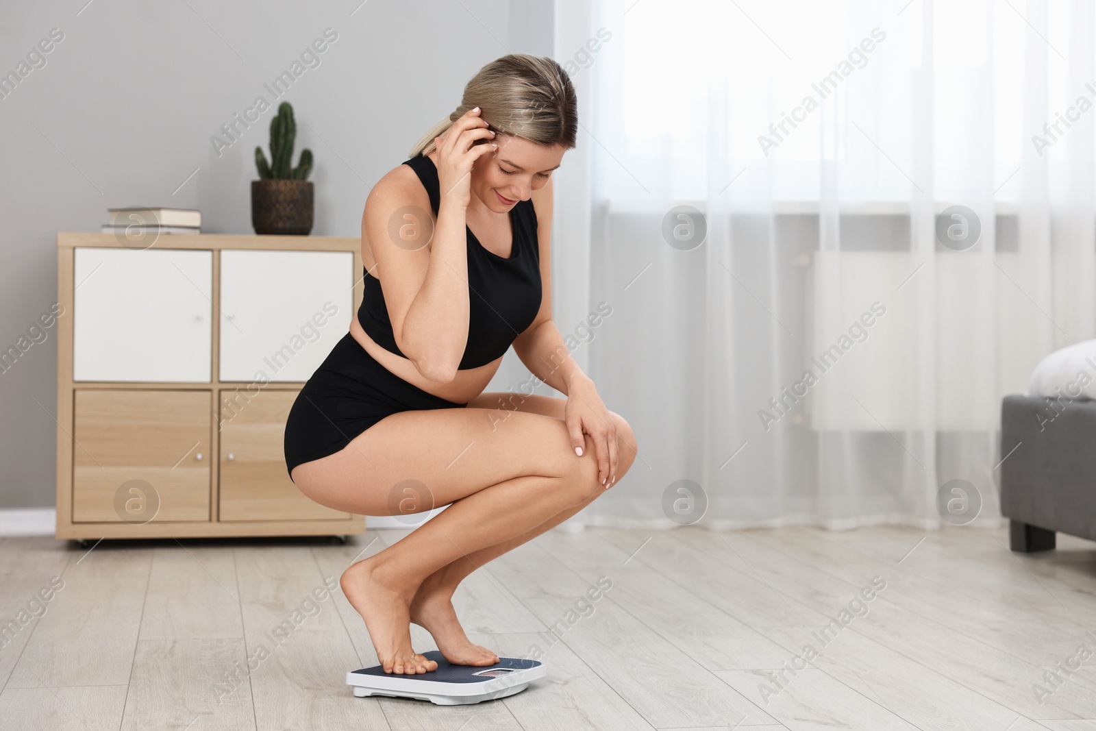 Photo of Happy woman standing on floor scales at home