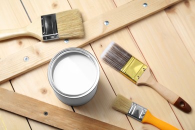 Photo of Can of white paint and brushes on wooden table, above view
