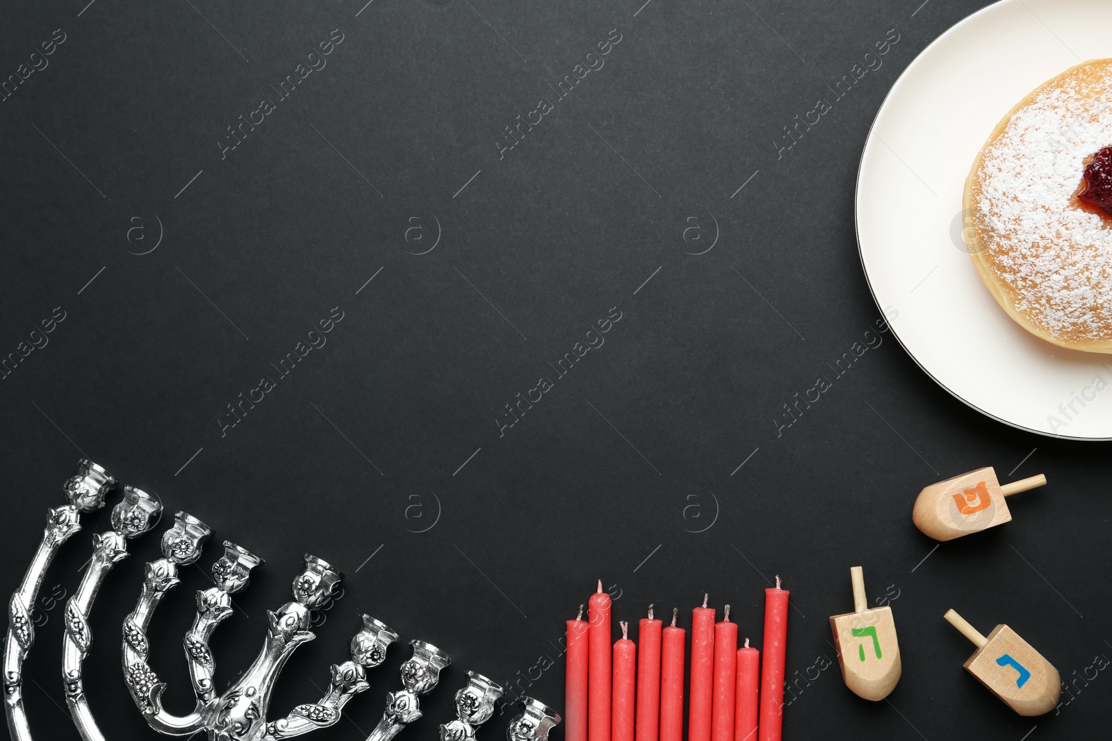 Photo of Hanukkah traditional menorah, candles, doughnut and dreidels with letters He, Pe, Nun, Gimel on black background, flat lay. Space for text