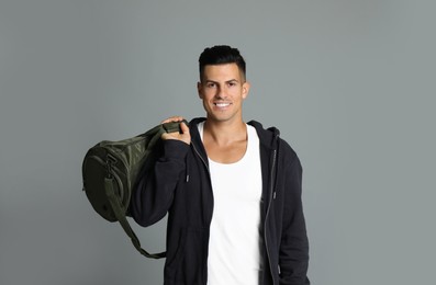 Handsome man with sports bag on grey background