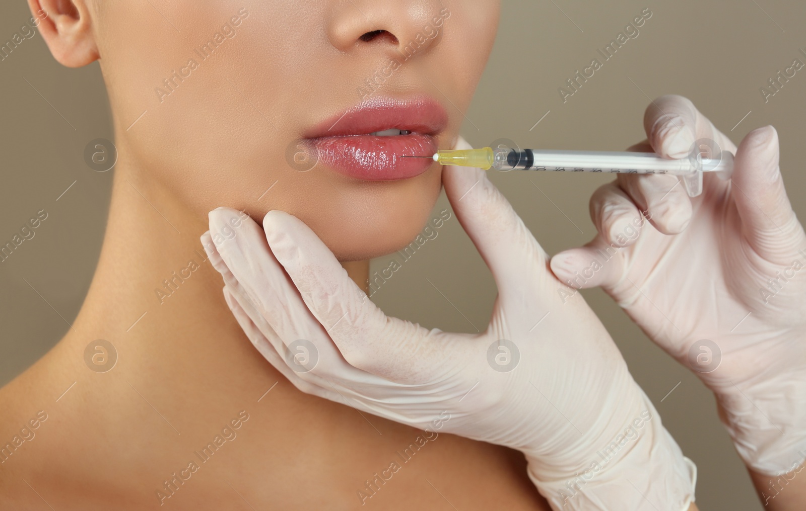 Photo of Woman getting lip injection on beige background, closeup