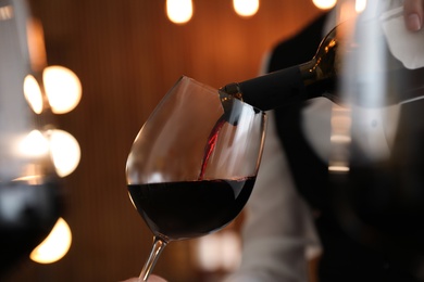 Waitress pouring wine into glass in restaurant, closeup