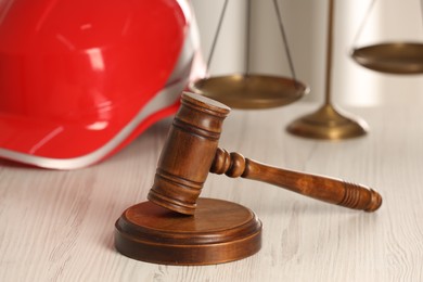 Photo of Law concept. Gavel, scales and red hard hat on white wooden table, closeup