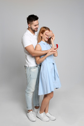 Man with engagement ring making marriage proposal to girlfriend on light grey background