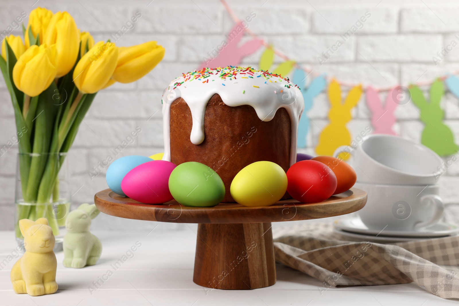 Photo of Stand with tasty Easter cake and decorated eggs on white wooden table