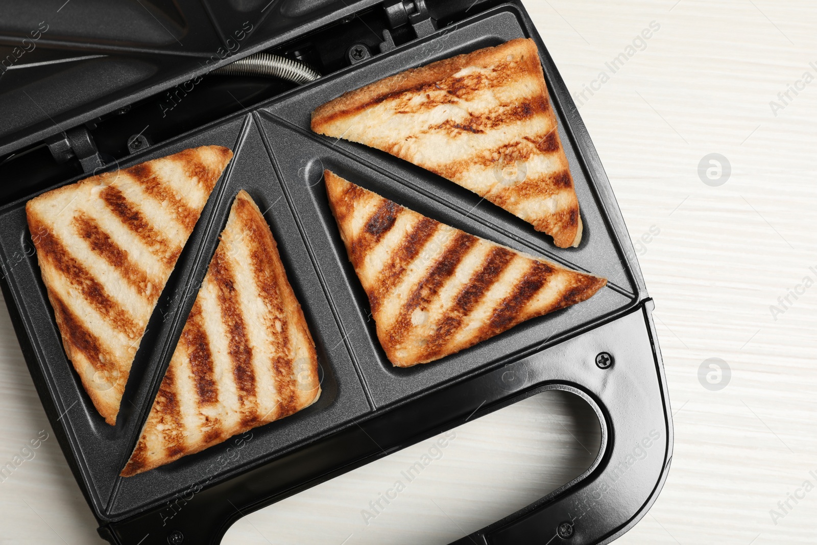 Photo of Modern sandwich maker with bread slices on white wooden table, top view