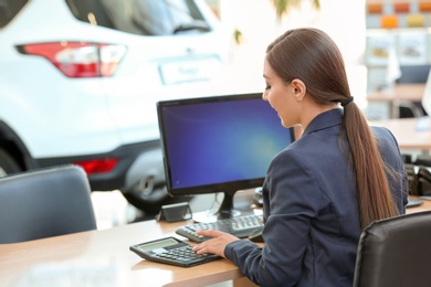 Young saleswoman sitting at table in car salon