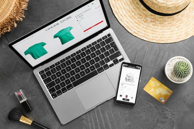 Online store website on laptop screen. Computer, smartphone, credit card, accessories and cactus on grey table, flat lay