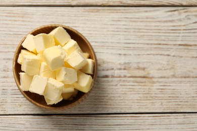 Photo of Tasty butter cubes in bowl on light wooden table, top view. Space for text