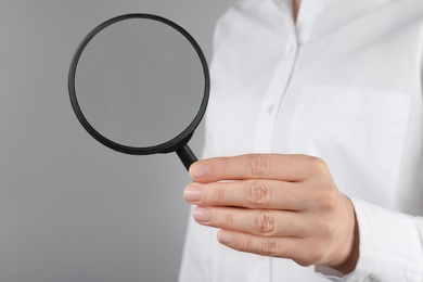 Woman holding magnifying glass on grey background, closeup. Find keywords concept