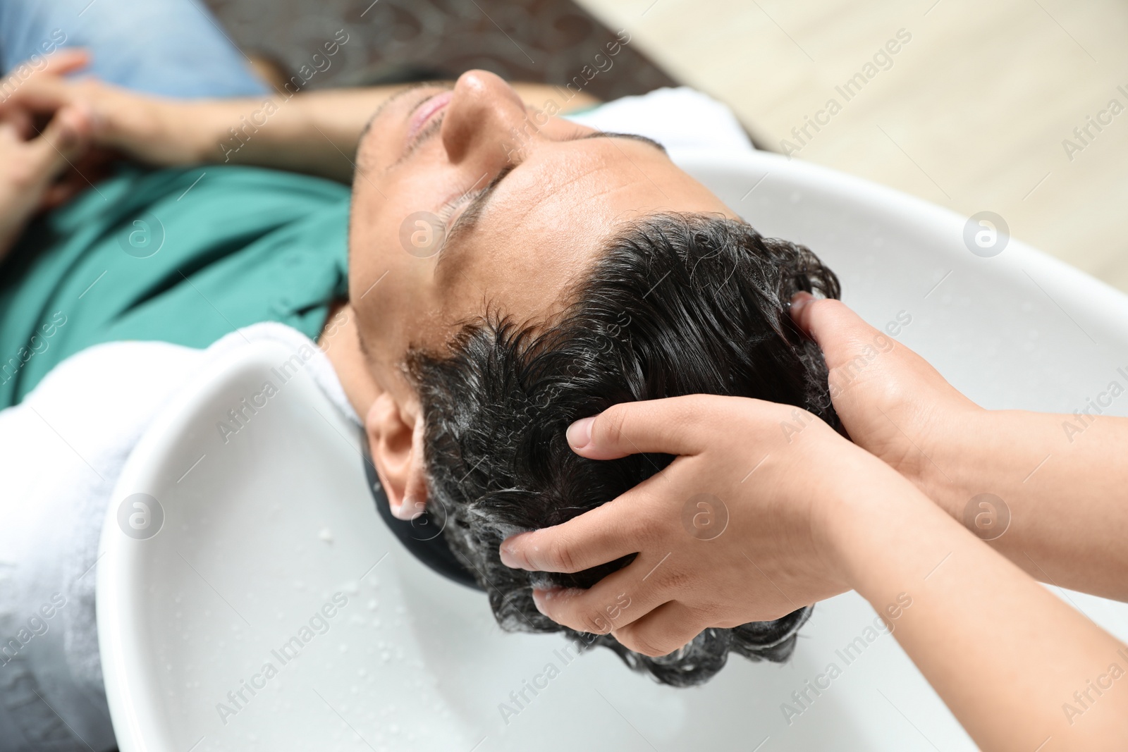 Photo of Stylist washing client's hair at sink in beauty salon