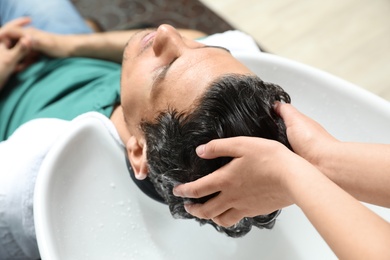 Photo of Stylist washing client's hair at sink in beauty salon